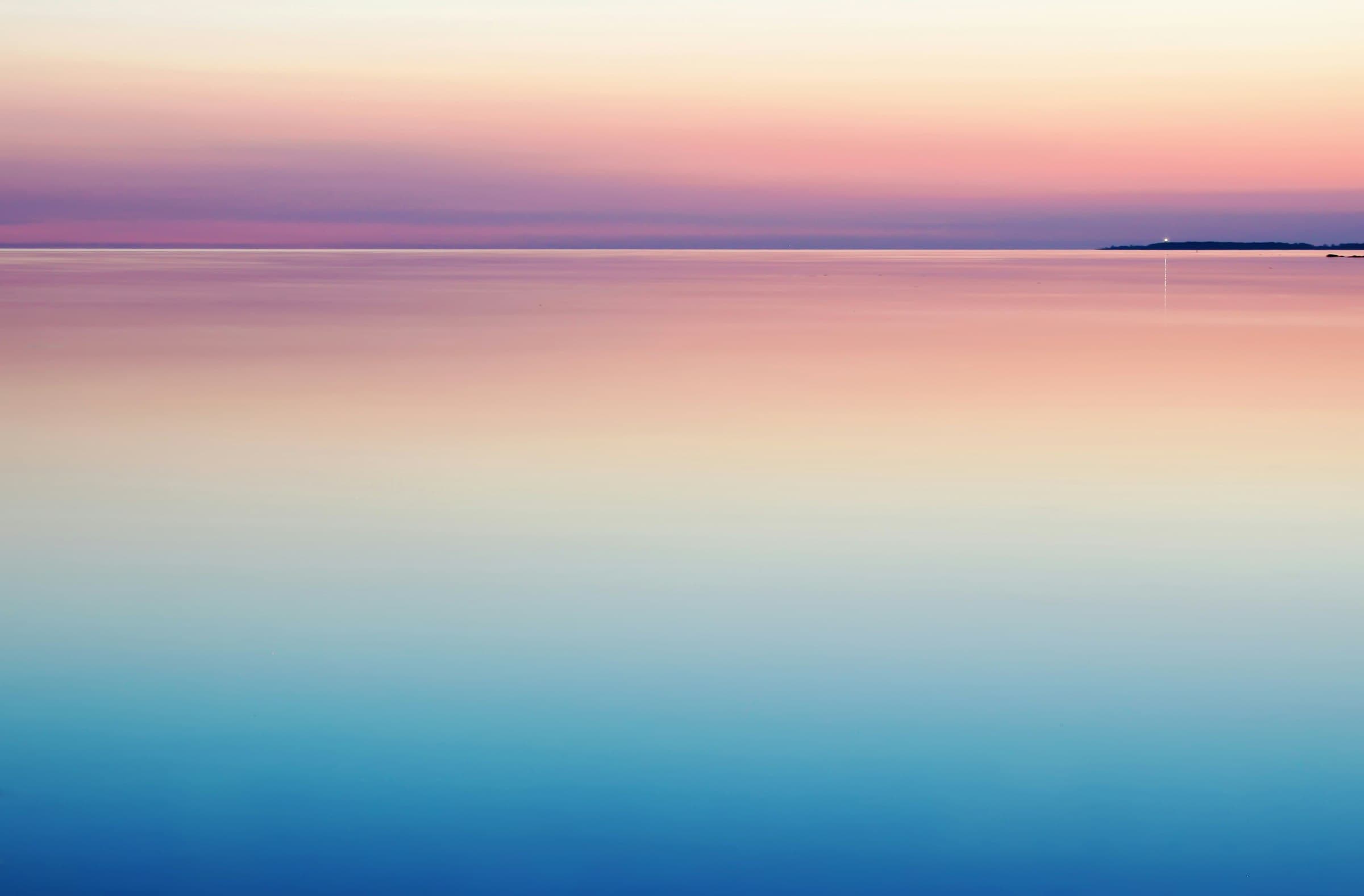 A calm sea at dawn, a lighthouse light just visible on the horizon